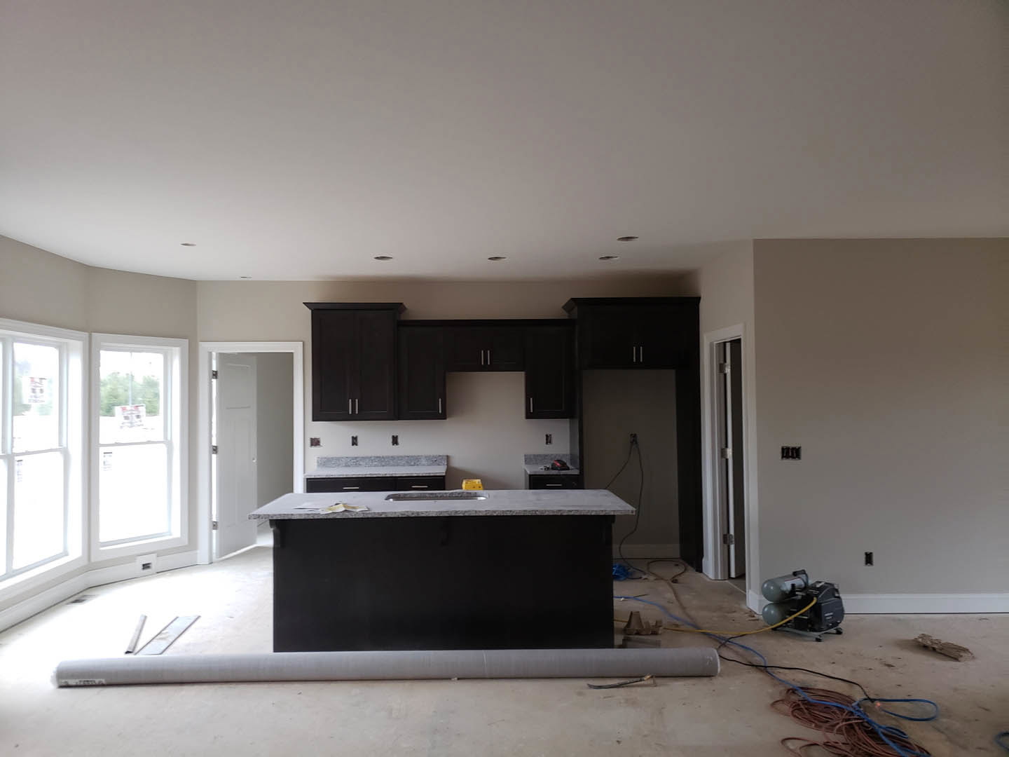 Modern kitchen with white cabinetry, stone countertop featuring a cutout for sink installation, roll of carpet on the floor, stainless steel appliances, and large window with a