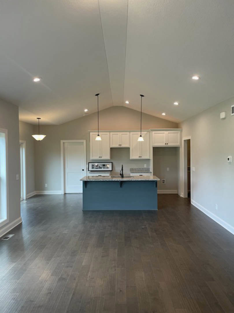 Open kitchen and dining area featuring hardwood flooring, blue accent wall, white door with black handle, modern cabinetry, light fixture, and plaster ceiling.