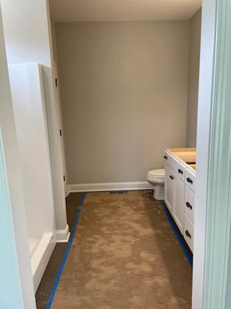 Modern bathroom with white toilet and rectangular sink, light-colored cabinetry, neutral walls, and blue painter’s tape on the tile floor