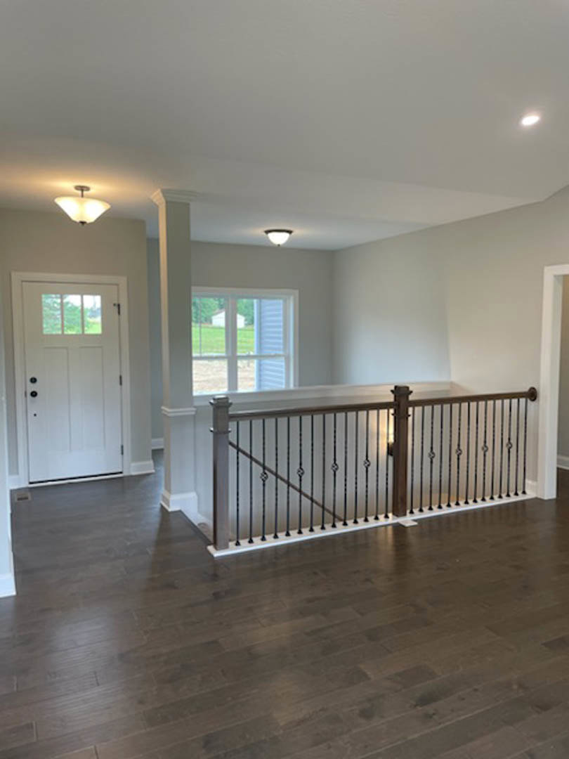 Dark wood flooring with a close-up of a metal railing, white door featuring a window, ceiling-mounted light fixture, and a window overlooking a green lawn.