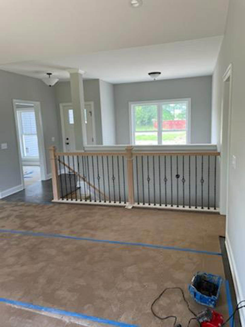 Open room featuring wood staircase with metal railing, large window overlooking green yard, laminate flooring, white plaster walls, black wire on floor, blue storage box with black