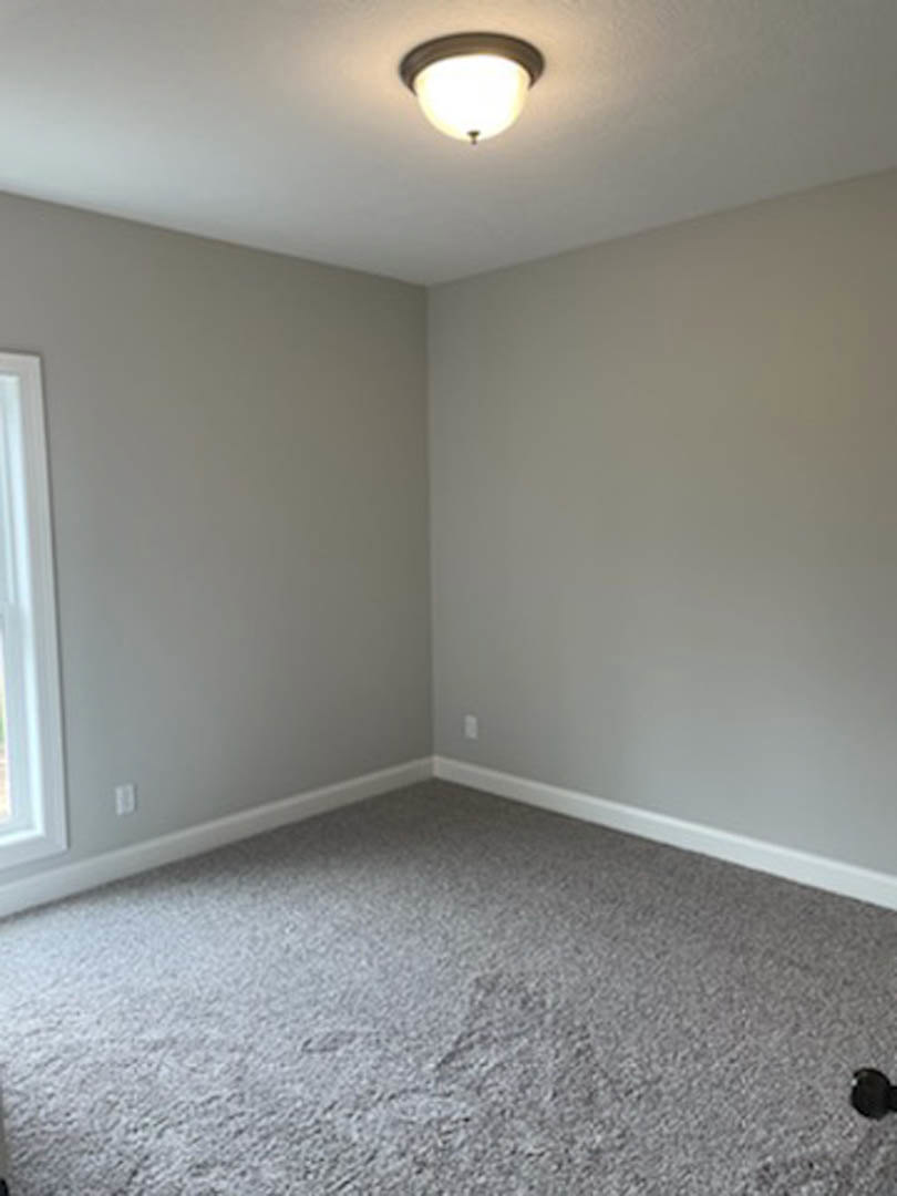 Bright room with white walls, white-framed window, grey carpet flooring, and modern ceiling light fixture