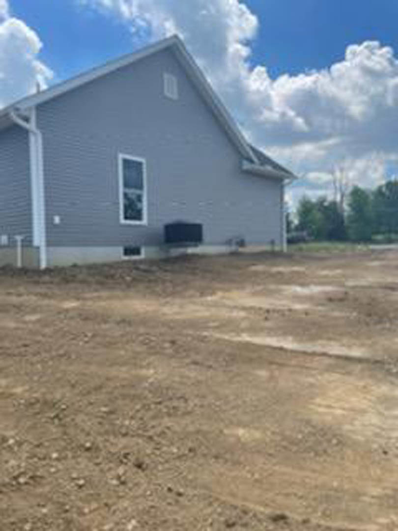 Two-story home with white siding and dark roof, large windows with white frames, set on a dirt lot under a blue sky with scattered clouds