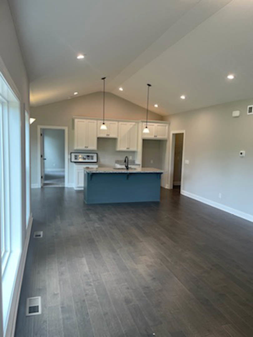 Open kitchen and dining area featuring wood flooring, white cabinetry, stone countertops, and large windows with white frames.