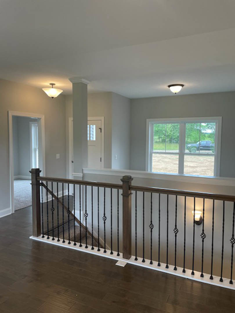 Wood staircase with metal handrail, laminate flooring, white walls, ceiling light fixture, large window showing parked truck outside