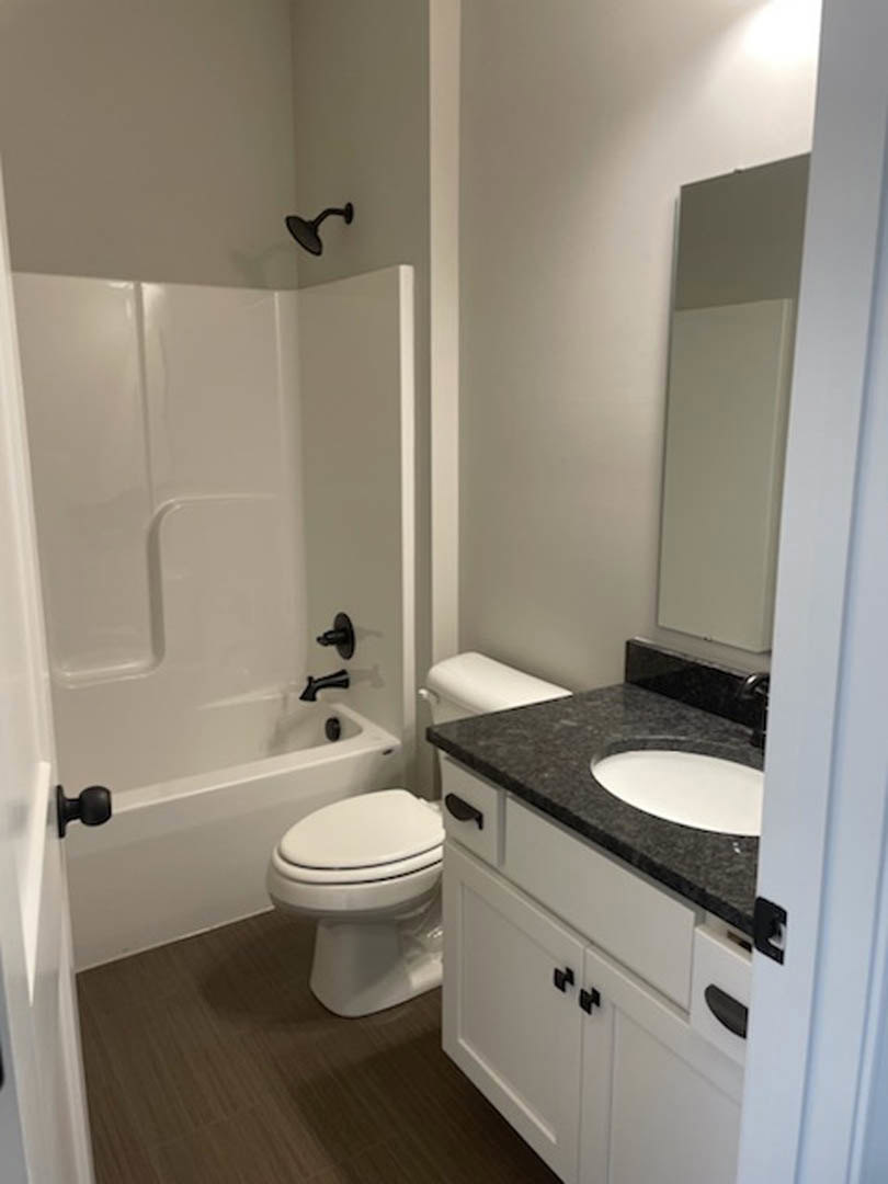 Modern bathroom featuring a white ceramic sink with chrome faucet, white toilet with closed lid, light gray tile flooring, and a black wall-mounted light fixture.