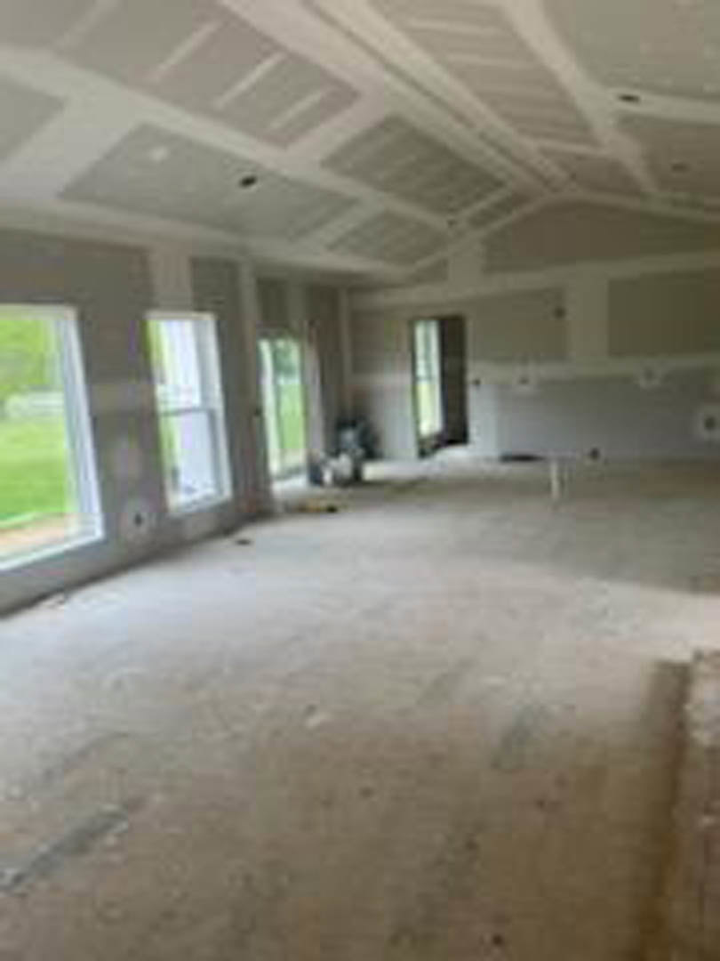 Spacious living area with high plaster ceiling, expansive windows, light-colored walls, and hardwood flooring