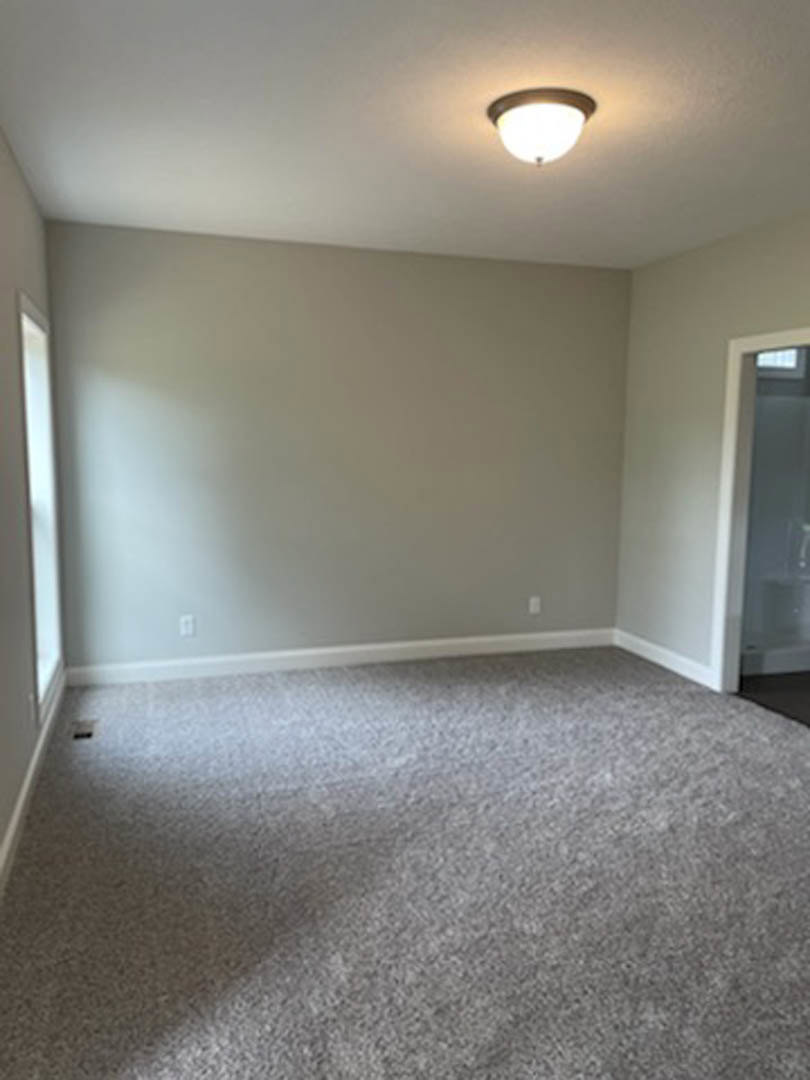 Carpeted room with white walls, white door, ceiling-mounted light fixture, and window in the background