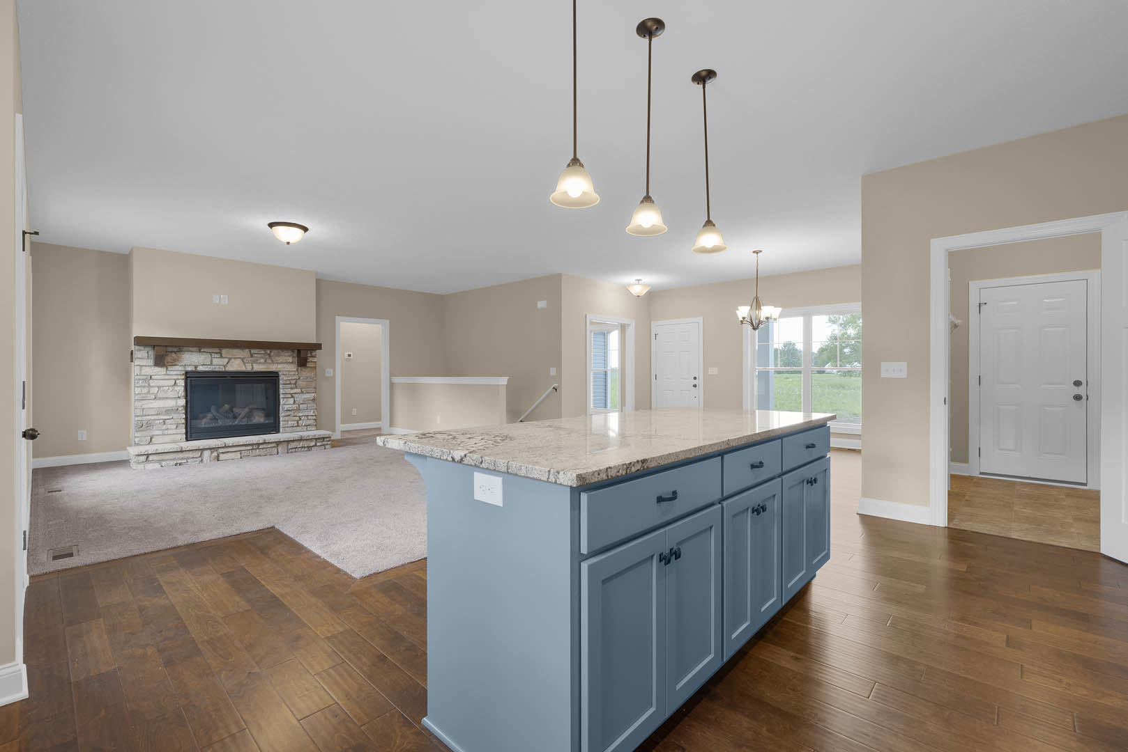 Marble-topped kitchen island with dark cabinetry, stainless steel appliances, white door with silver doorknob, fireplace with glass door, hardwood flooring, and light-colored walls