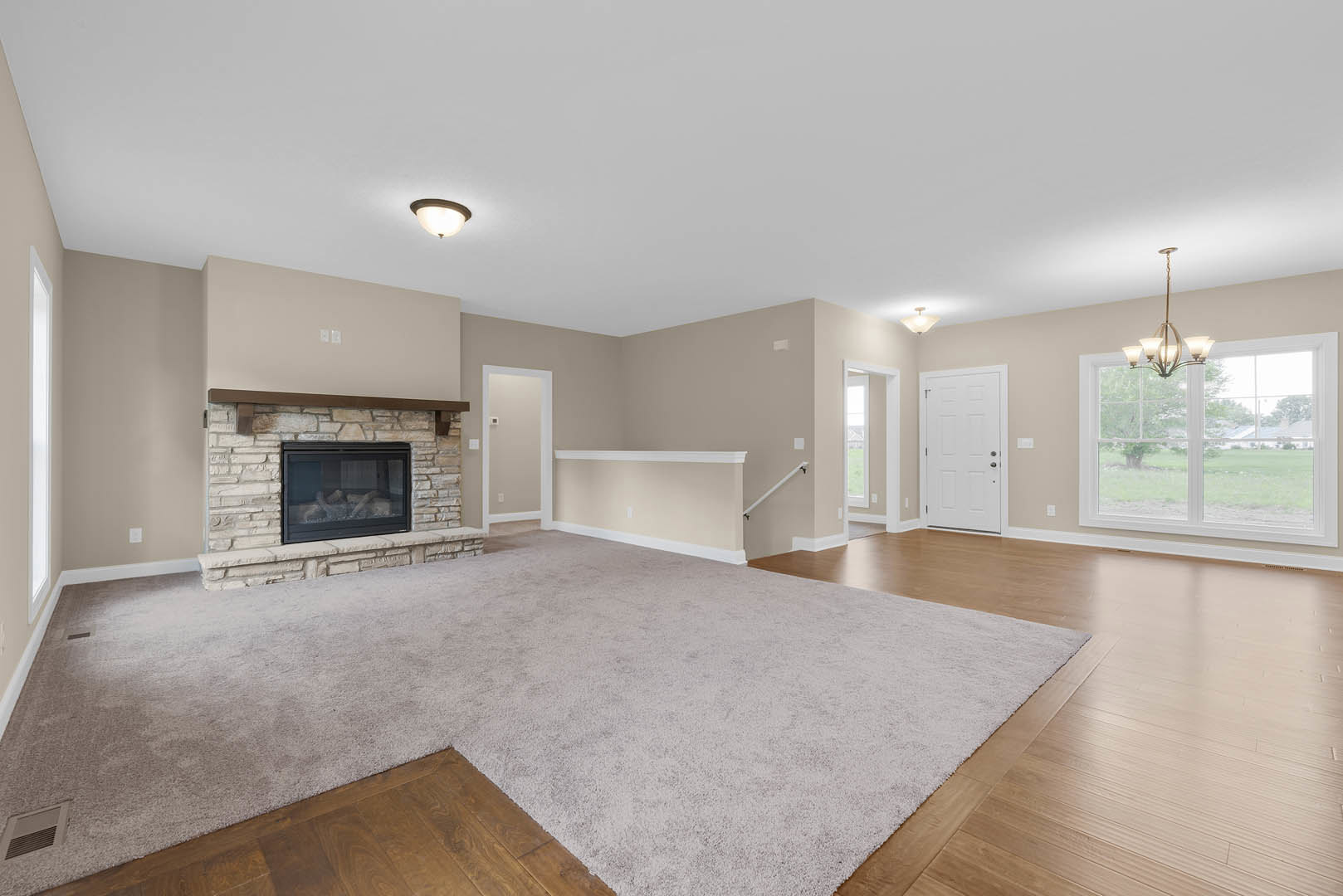 Living room with hardwood floors, glass-door fireplace, area rug, chandelier near large window, white door with matching handle, plaster walls and ceiling