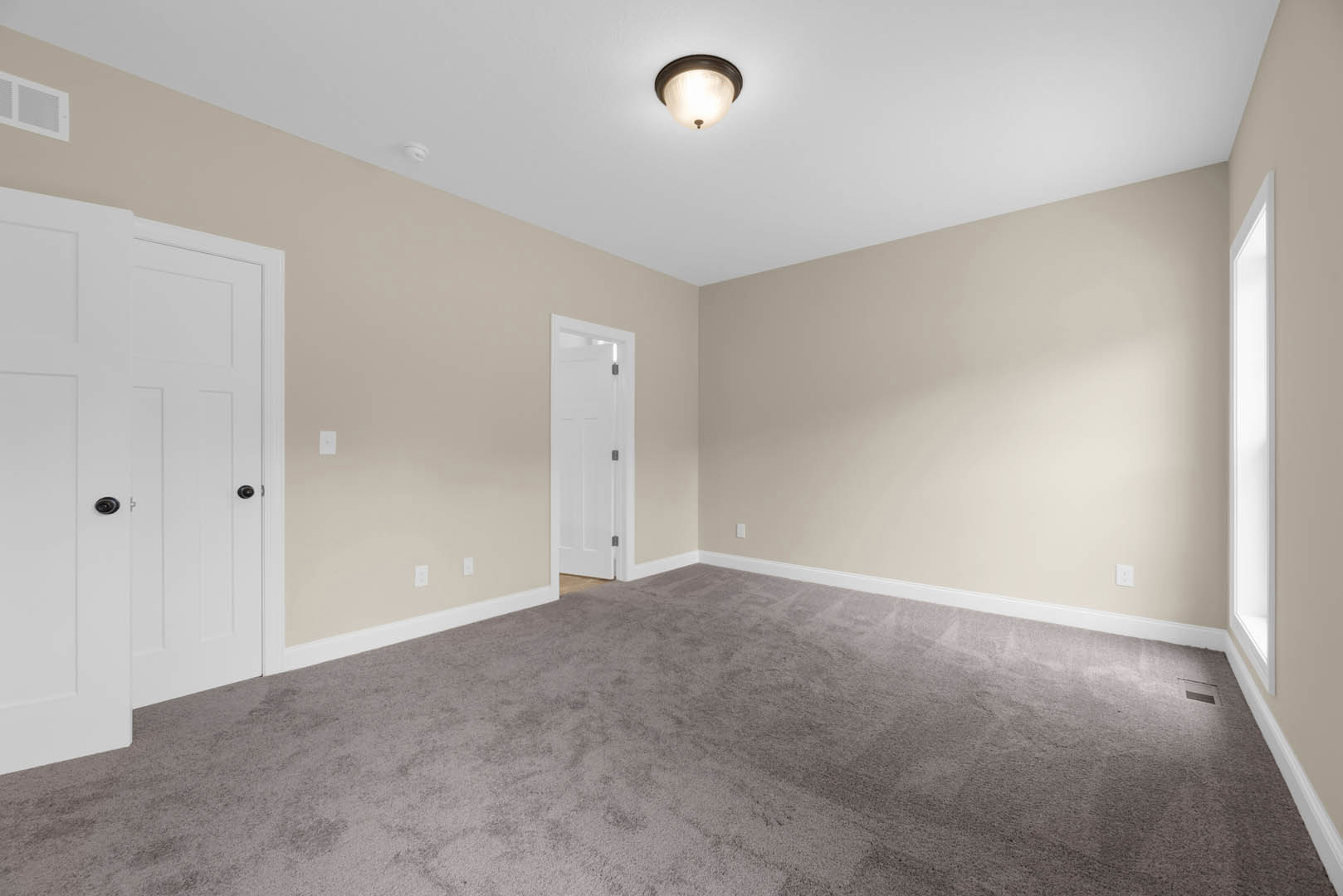Beige-walled room with plush carpet, white paneled doors, and a ceiling-mounted light fixture