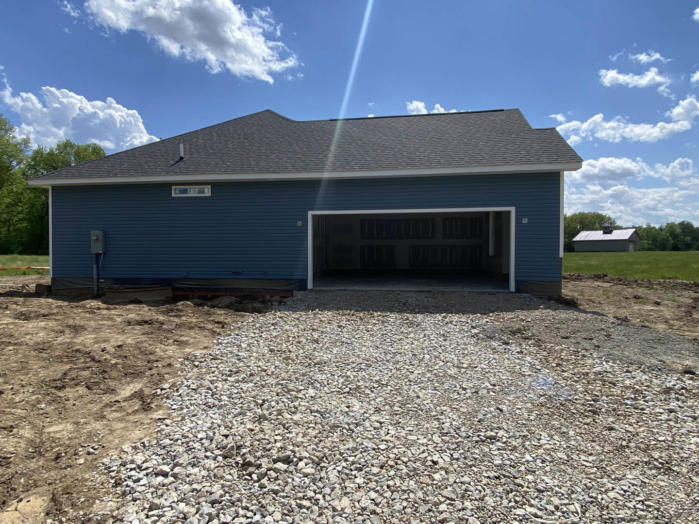 Blue siding garage with white trim, gravel driveway in front, cloudy sky above, trees and land lot surrounding the building