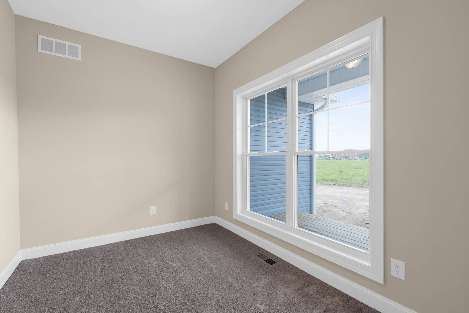 Neutral-toned carpeted floor, white walls, large window with blinds, wall outlet and air vent visible