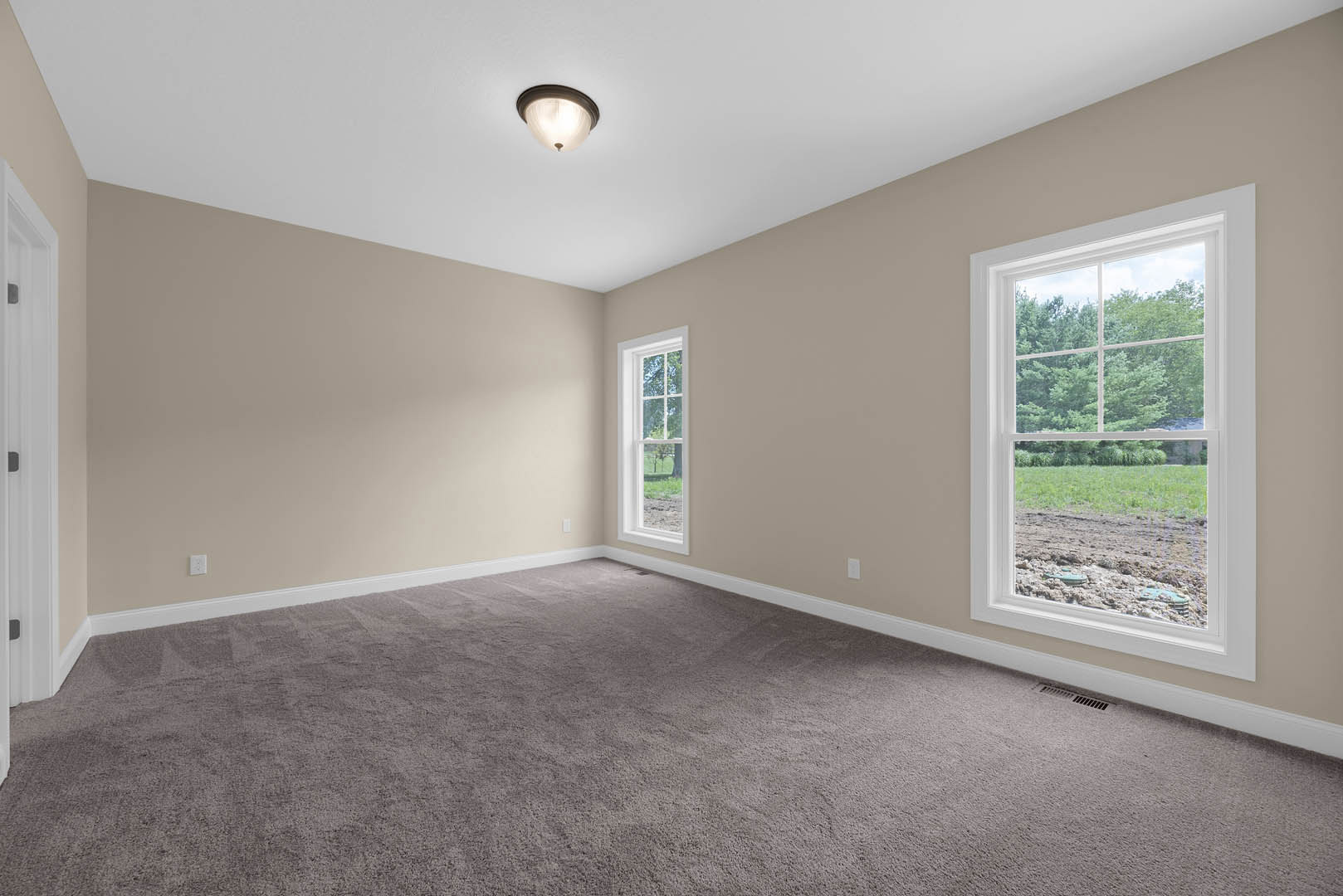 Bedroom with beige carpet, white walls, ceiling light fixture, and large window overlooking grassy field and trees