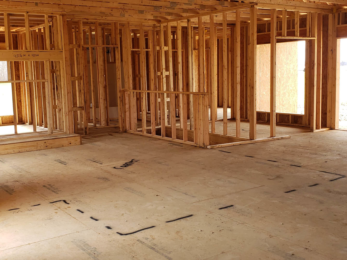 Exposed wood framing with beams, unfinished walls, and subfloor marked with black writing inside a house under construction