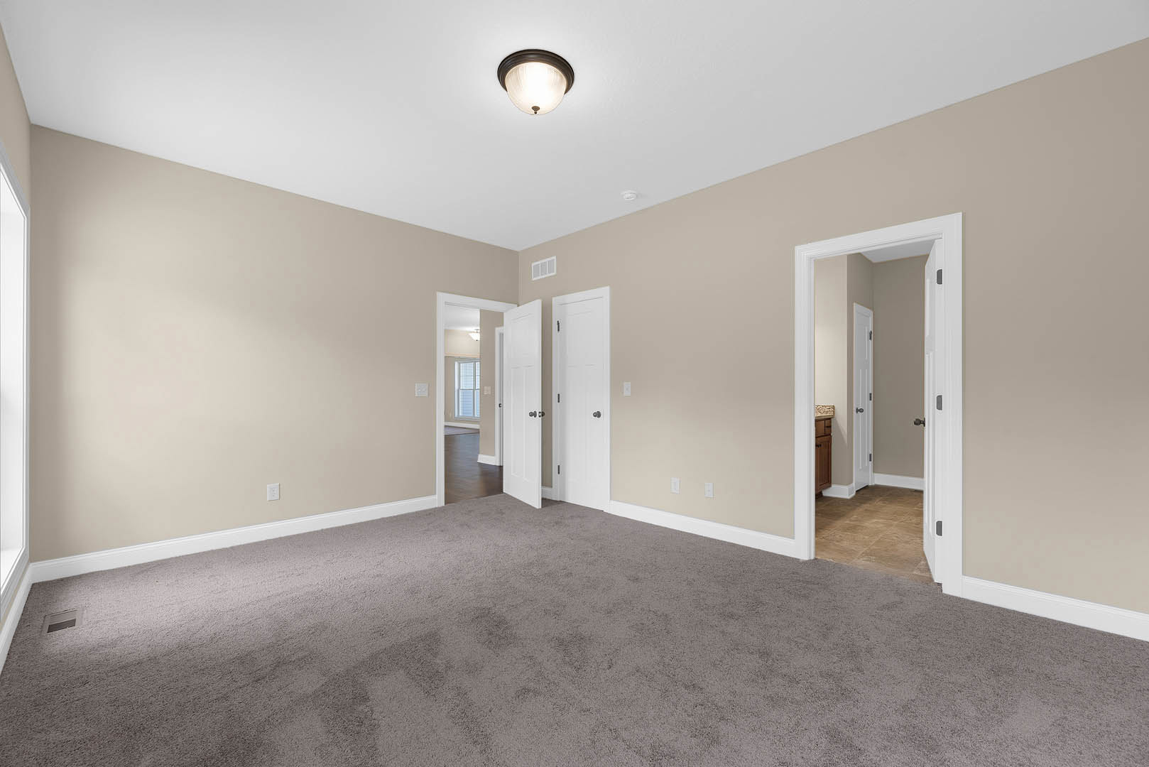 Beige walls and carpeted floor, white doors with silver doorknobs, ceiling light fixture, hallway with white trim and molding