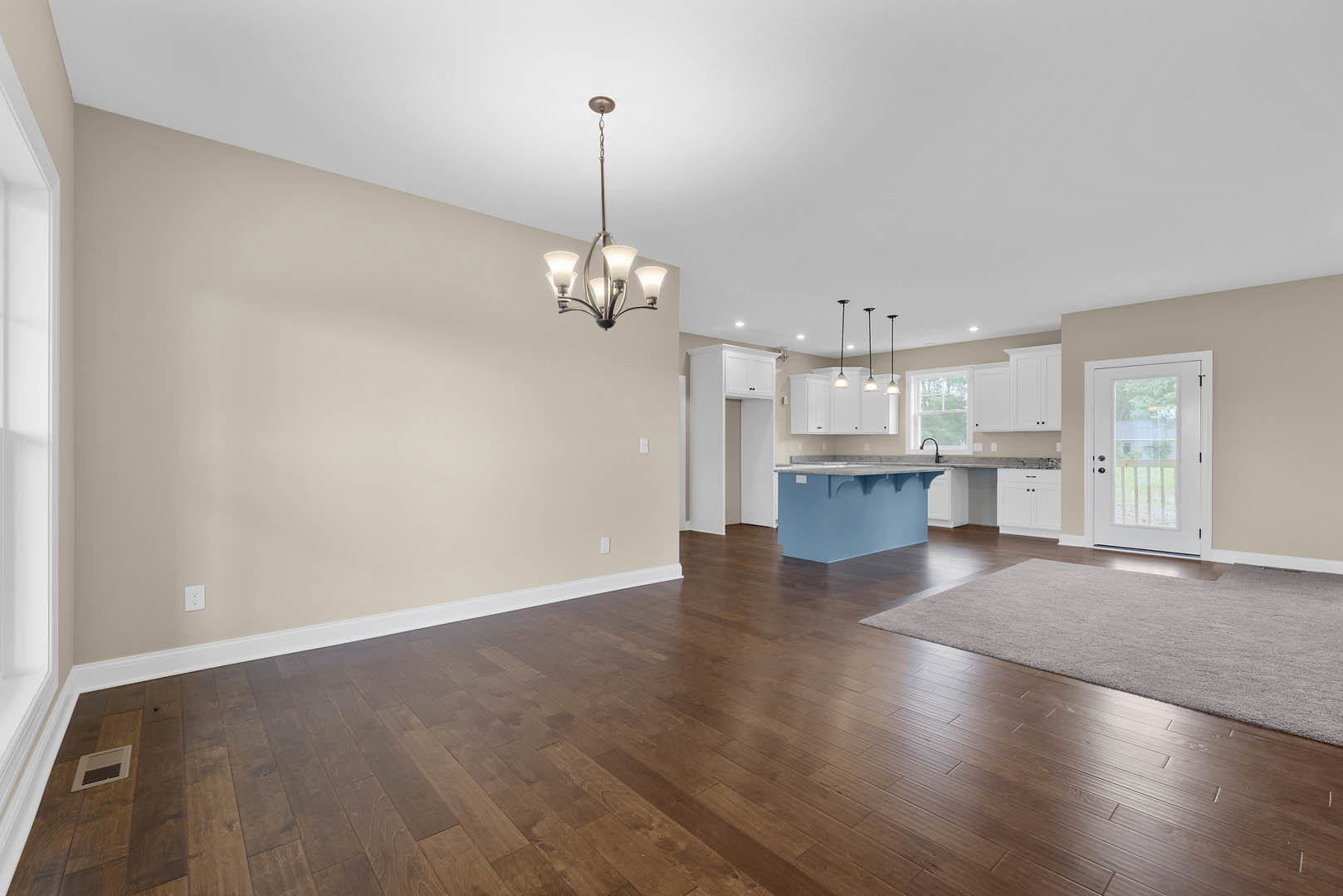 Open-concept kitchen and dining area featuring a blue island with white countertop, hardwood flooring, white cabinetry, glass-paneled door, modern chandelier, and a patterned rug.