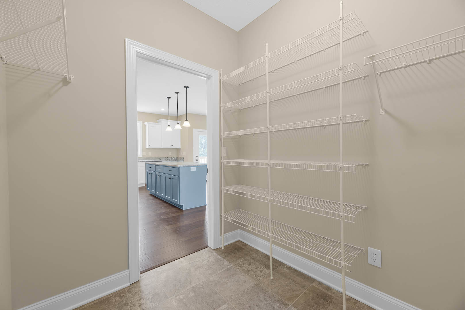 White built-in shelves on a plaster wall, recessed ceiling lights above, white cabinets and drawers below, light wood flooring, white electrical outlet visible.