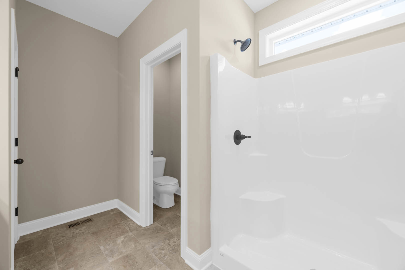 Modern bathroom featuring white tile shower with chrome showerhead, white toilet with closed lid, wall vent, recessed ceiling light, and plaster walls.
