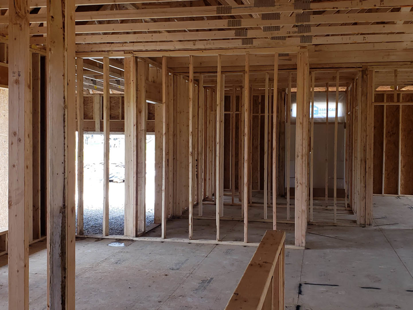 Exposed wood framing and beams inside a partially constructed house with concrete flooring, window opening, and construction materials visible
