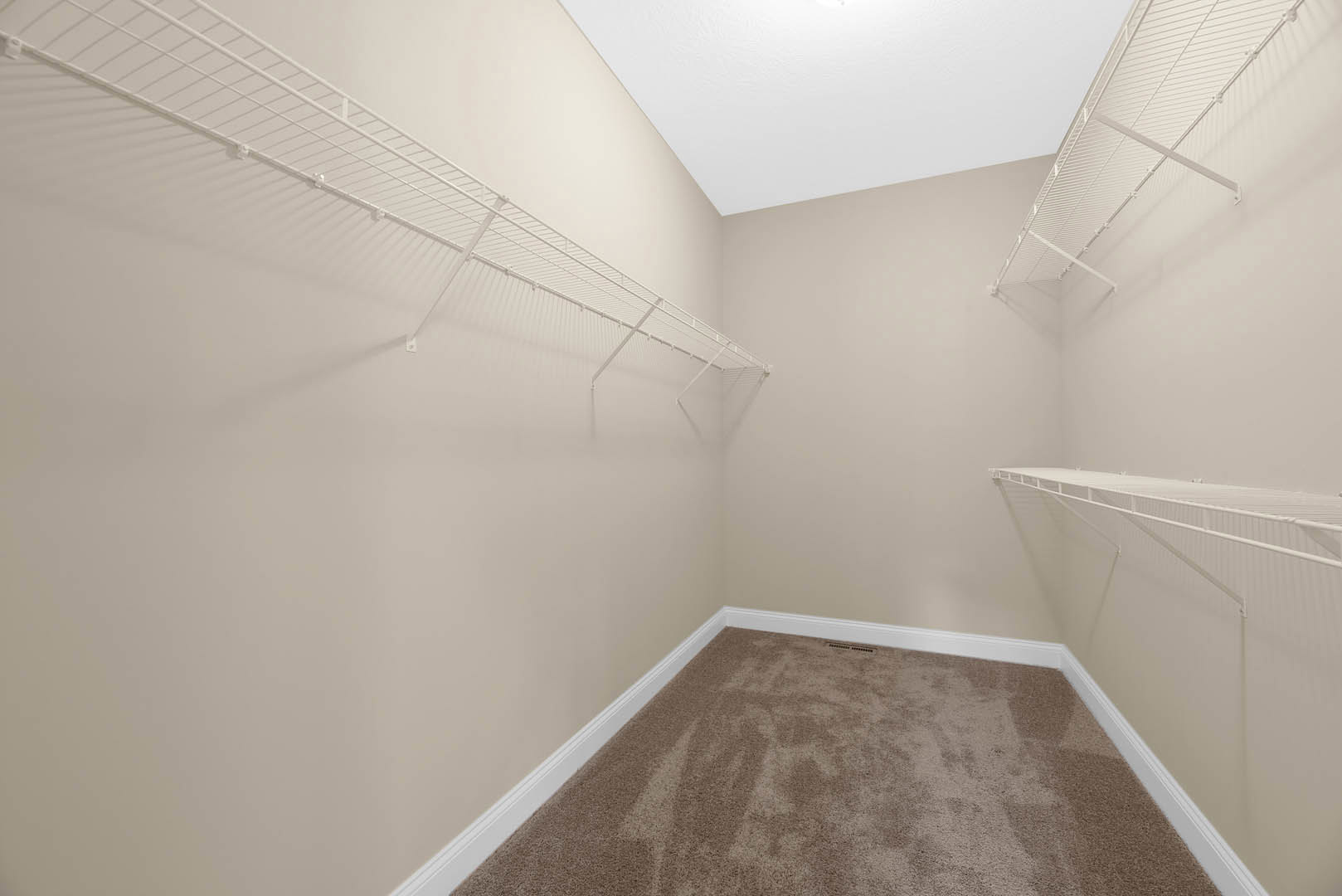Carpeted room with white wall-mounted shelves, ceiling vent, and person standing near the shelves