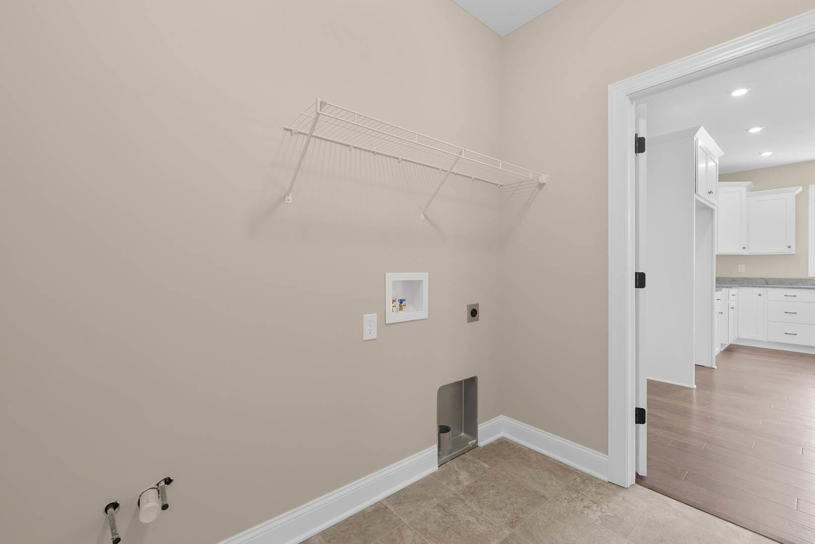 White wall-mounted rack with metal rods above hardwood flooring, metal canister in corner, white box with exposed valves, plaster walls, and ceiling in residential room.