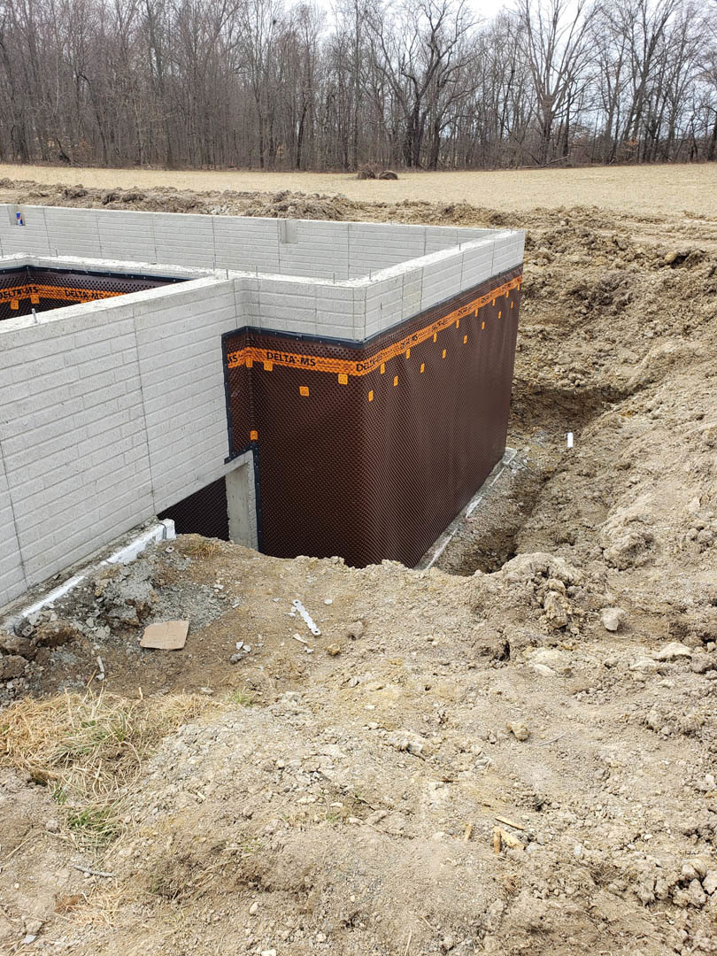 Concrete foundation slab surrounded by dirt, construction materials, and scattered trees under a clear sky