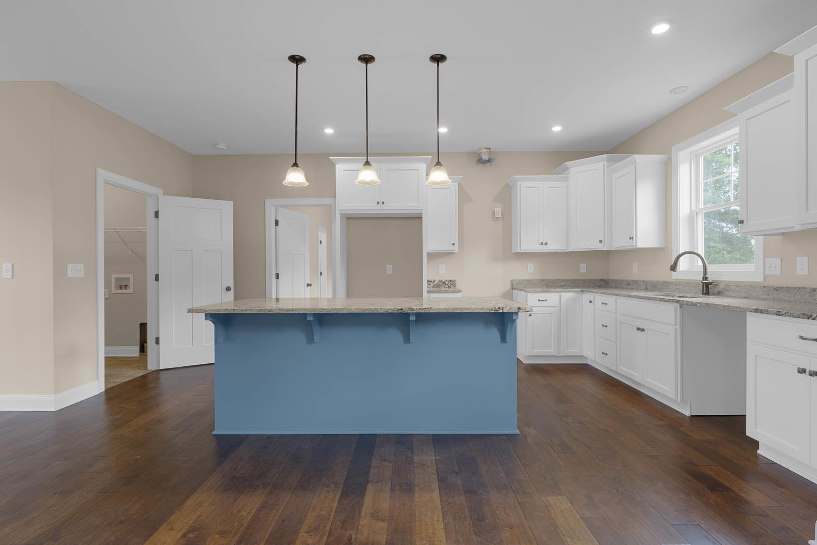 Blue kitchen island with marble countertop, white shaker cabinets, stainless steel appliances, wooden flooring, and light blue accent wall.