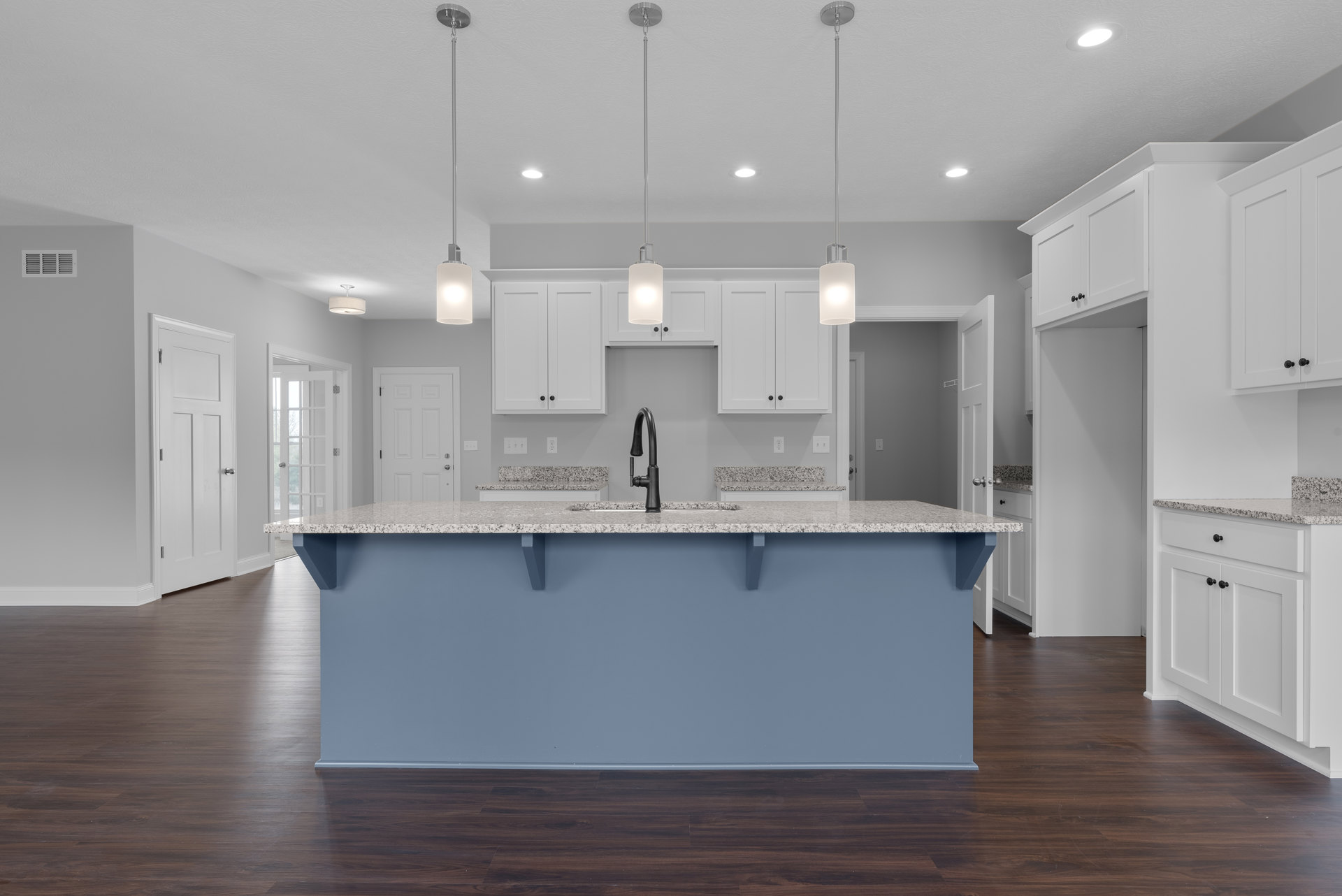 Blue kitchen island with white quartz countertop, tile backsplash, stainless steel sink and faucet, shaker cabinetry, pendant light fixture, hardwood flooring, and white door in
