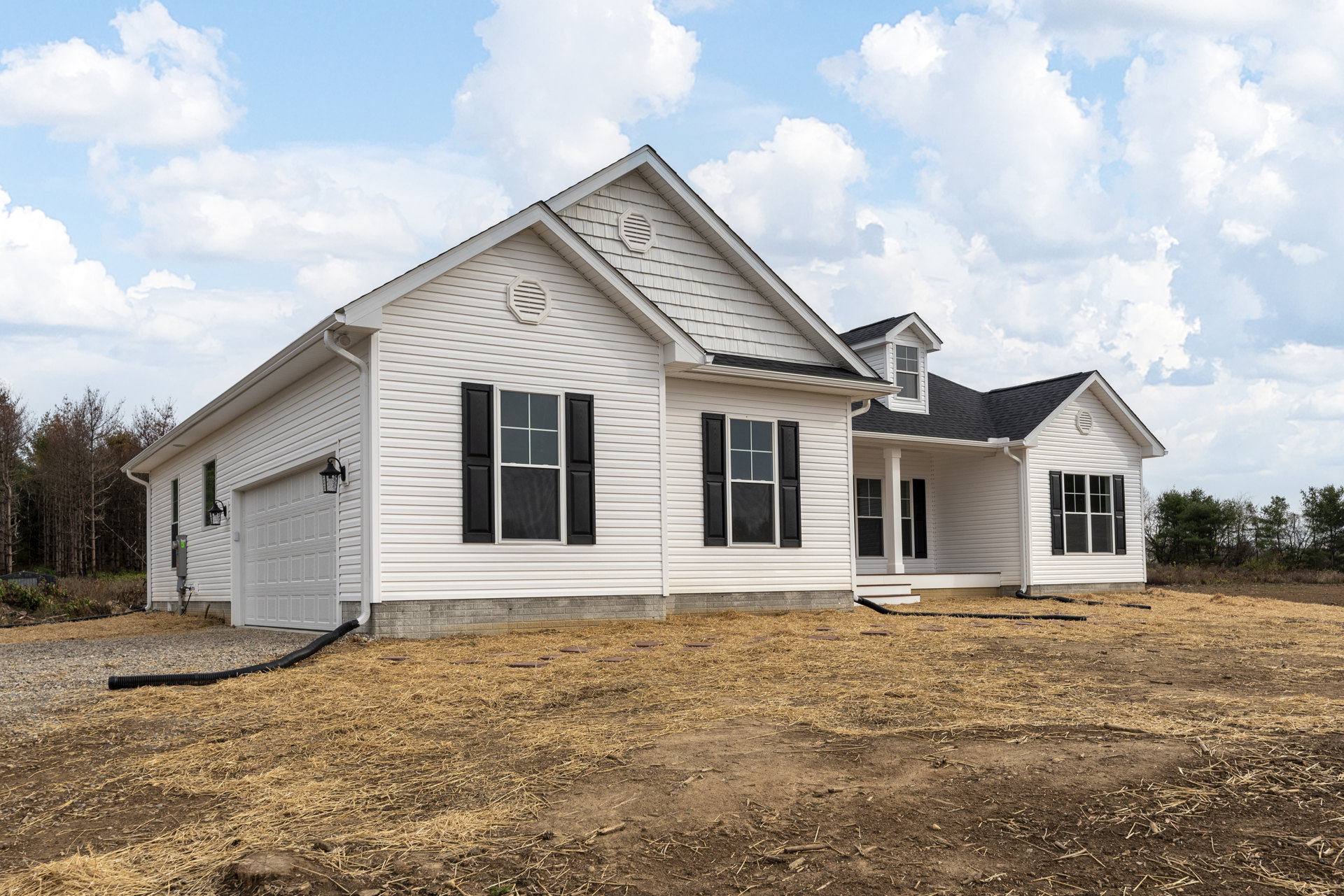 White house with black shutters and attached garage, set on a large dirt yard with straw, under a blue sky; Robert Frost Farm visible in the background.