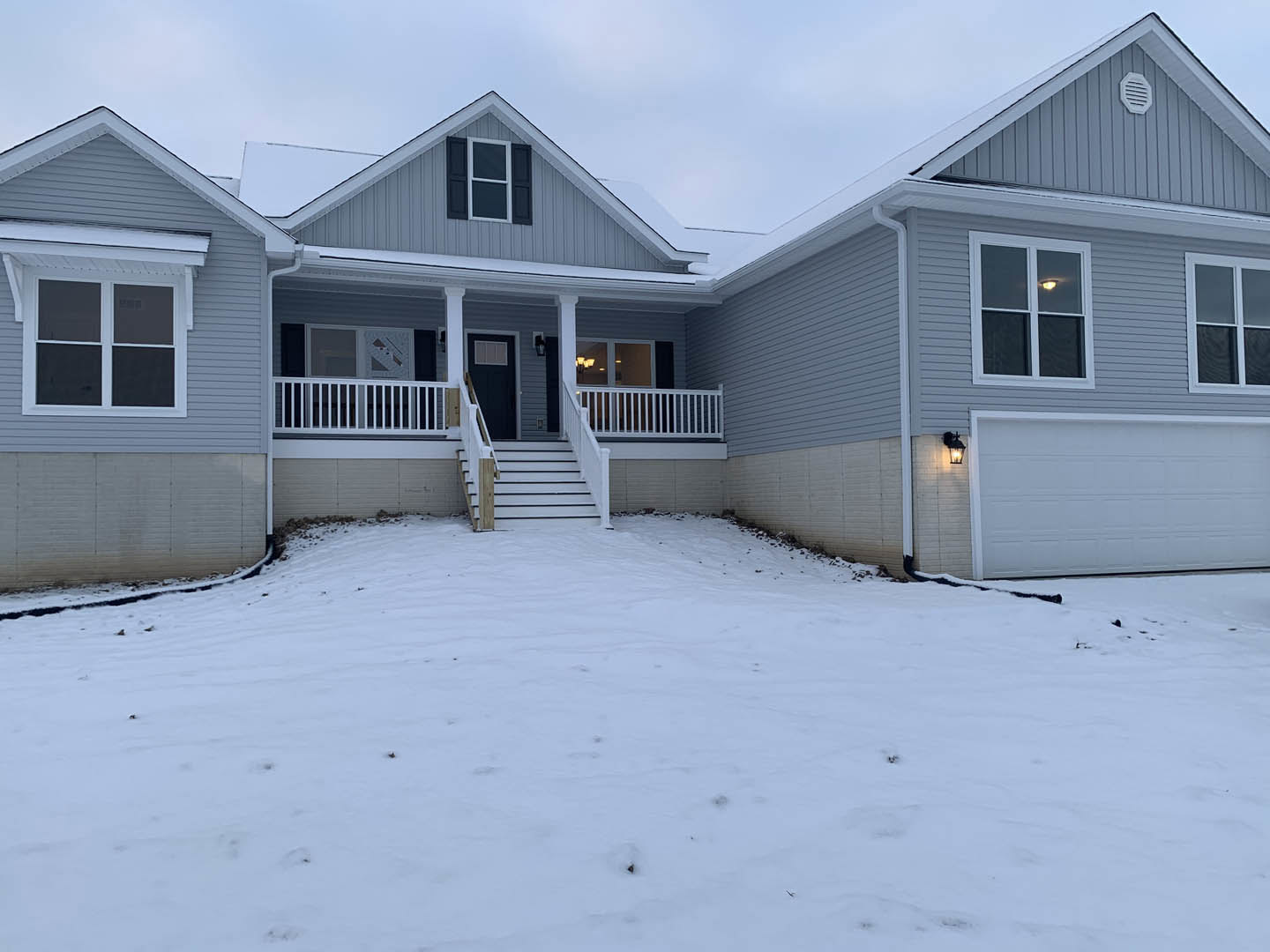 Two-story home with white siding, black roof, and white garage door; snow covers the ground and stairs leading to a porch with white railing featuring black stripes; large windows