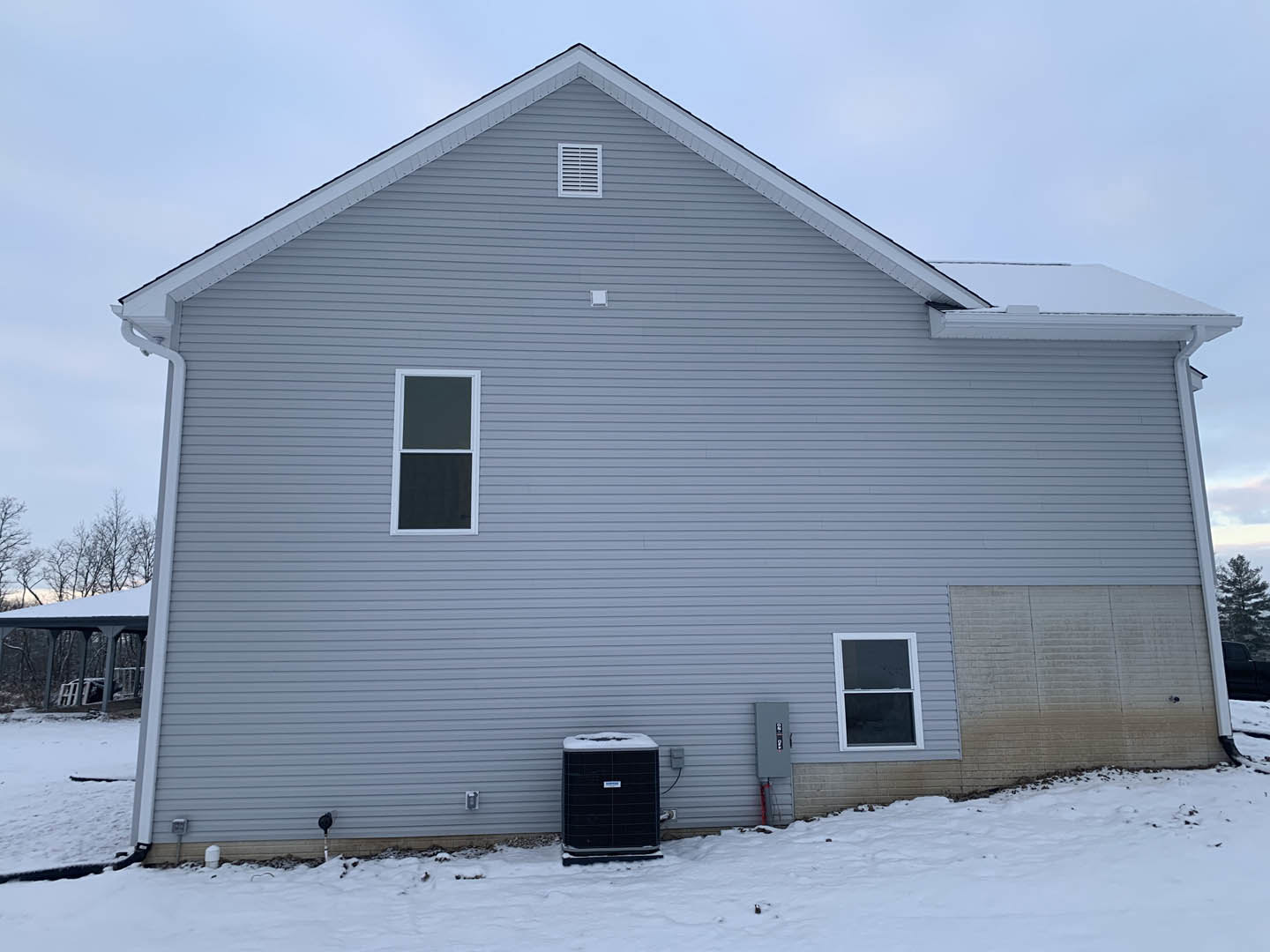 Two-story home with grey siding, white-framed windows, and snow-covered yard; black air conditioner sits near the foundation; historic Rockingham Meeting House visible in the