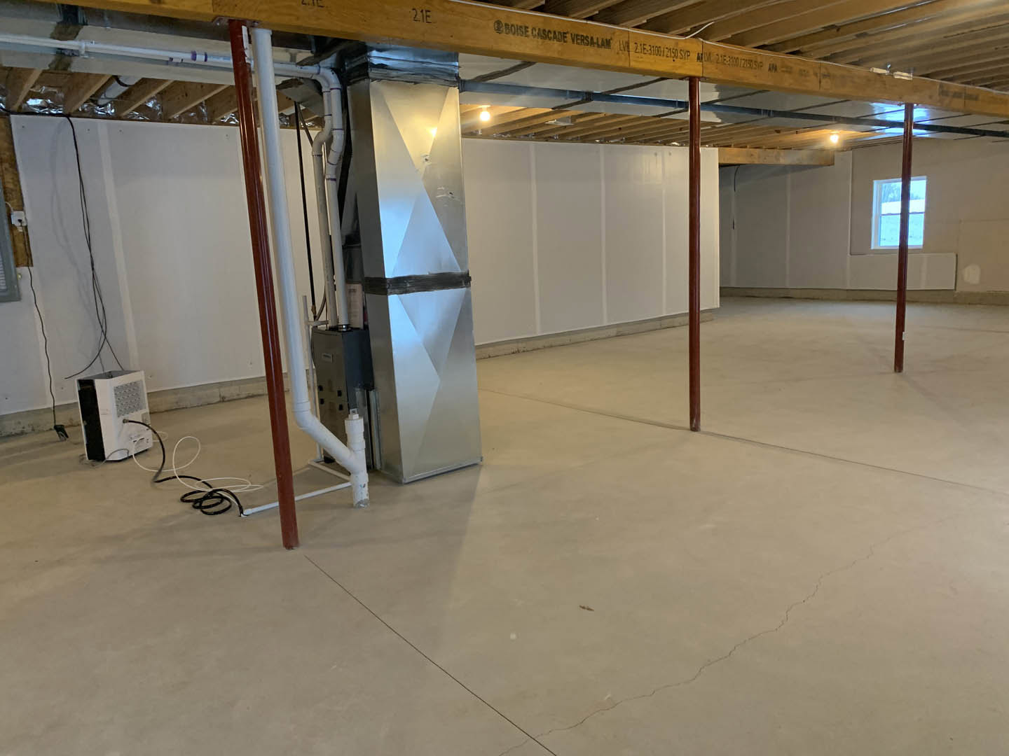 Spacious interior with exposed wood beam, plaster walls, light flooring, large metal box topped with black plastic bag, white box secured with black tape and wires, window framed