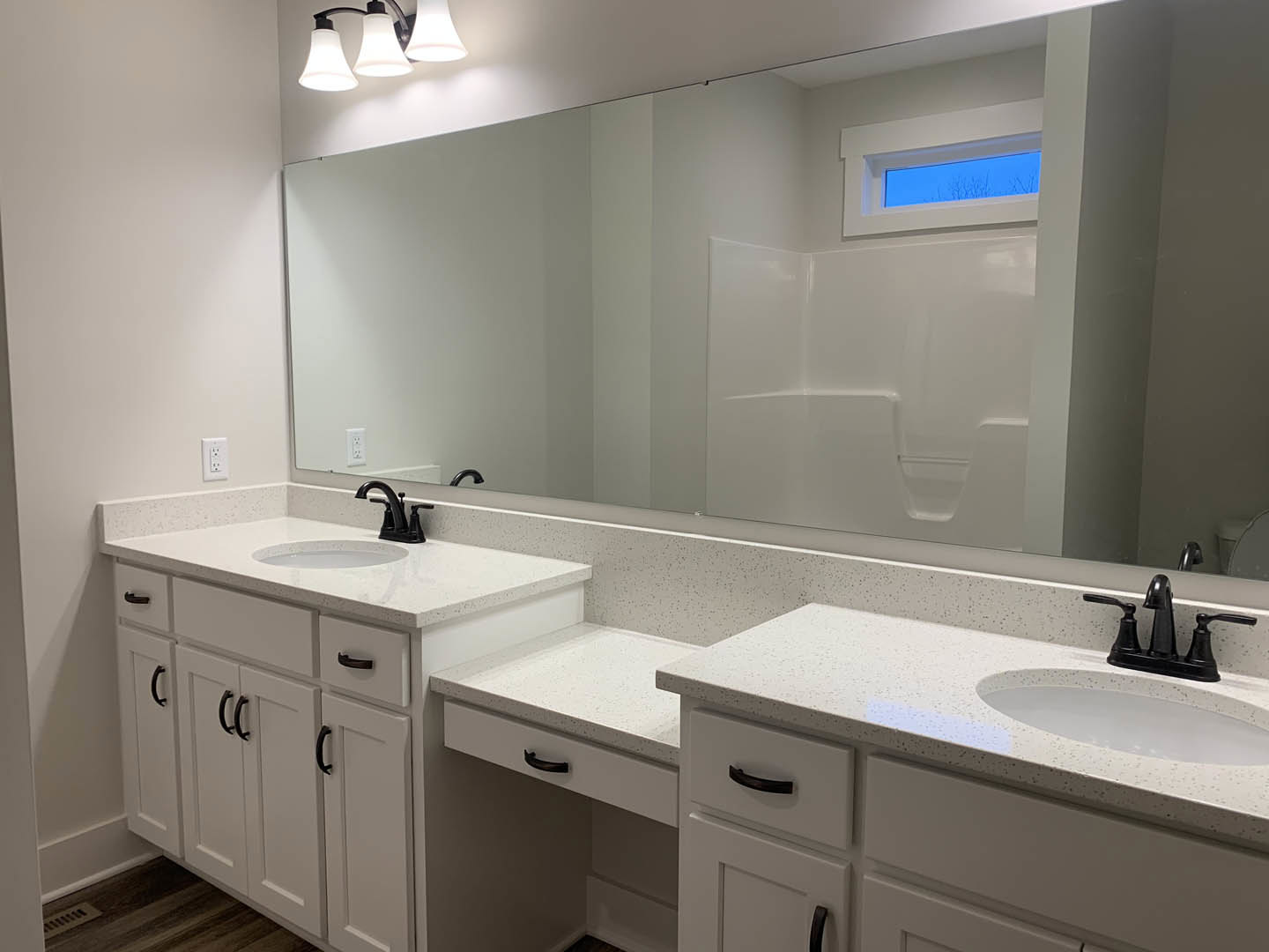 Bathroom featuring a large wall mirror, white countertop with black faucet, white sink with black handle, light fixture, window, and mirror above a white bathtub.
