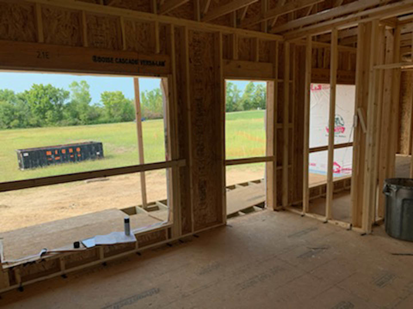 Spacious room featuring large windows, wood flooring, exposed beams, and a view of green grass and trees outside