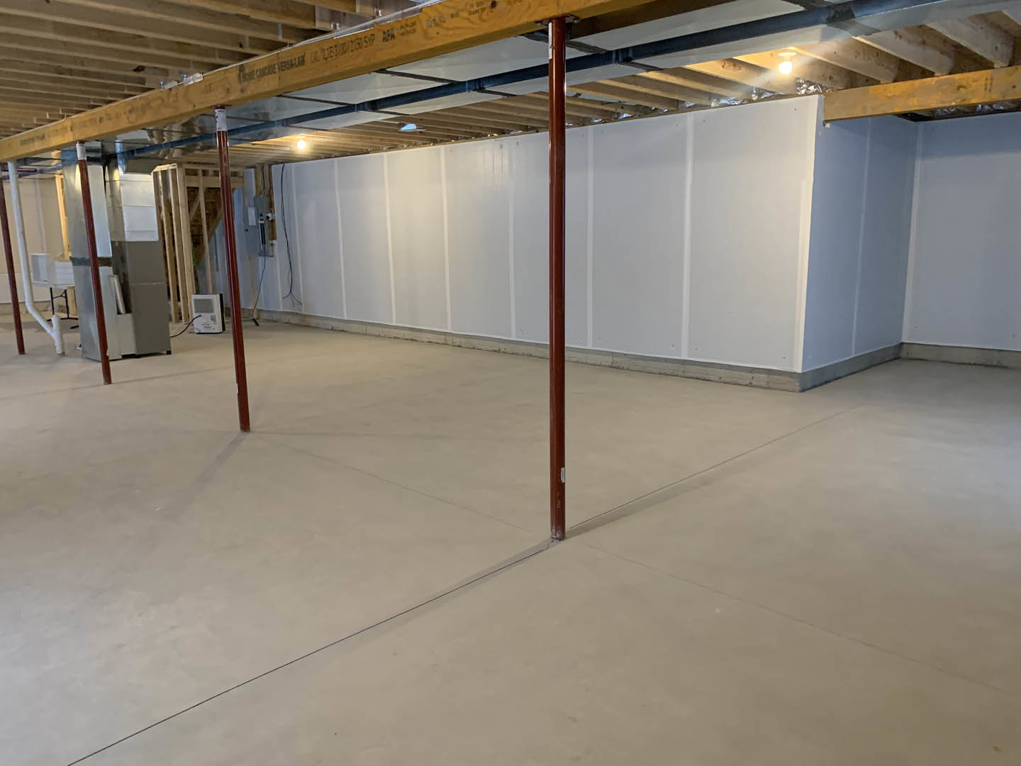 Open room with exposed wooden ceiling beam, white wall with black border, concrete floor, and metal support pole