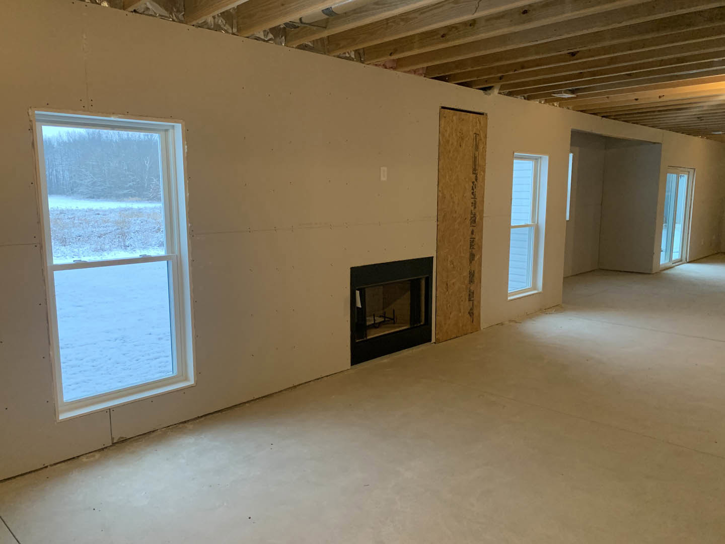 Living room with plaster walls, wide windows overlooking a snowy field, stone fireplace, and hardwood flooring