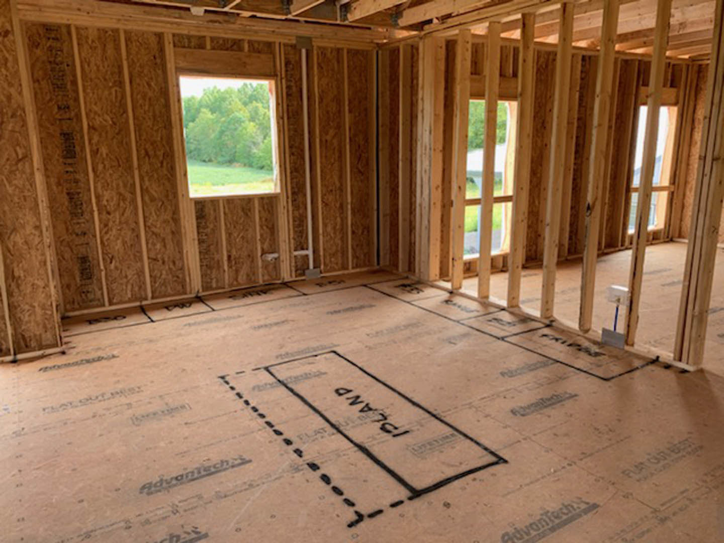 Room with wood plank walls, exposed wood beams, large window overlooking trees, unfinished flooring with black construction markings