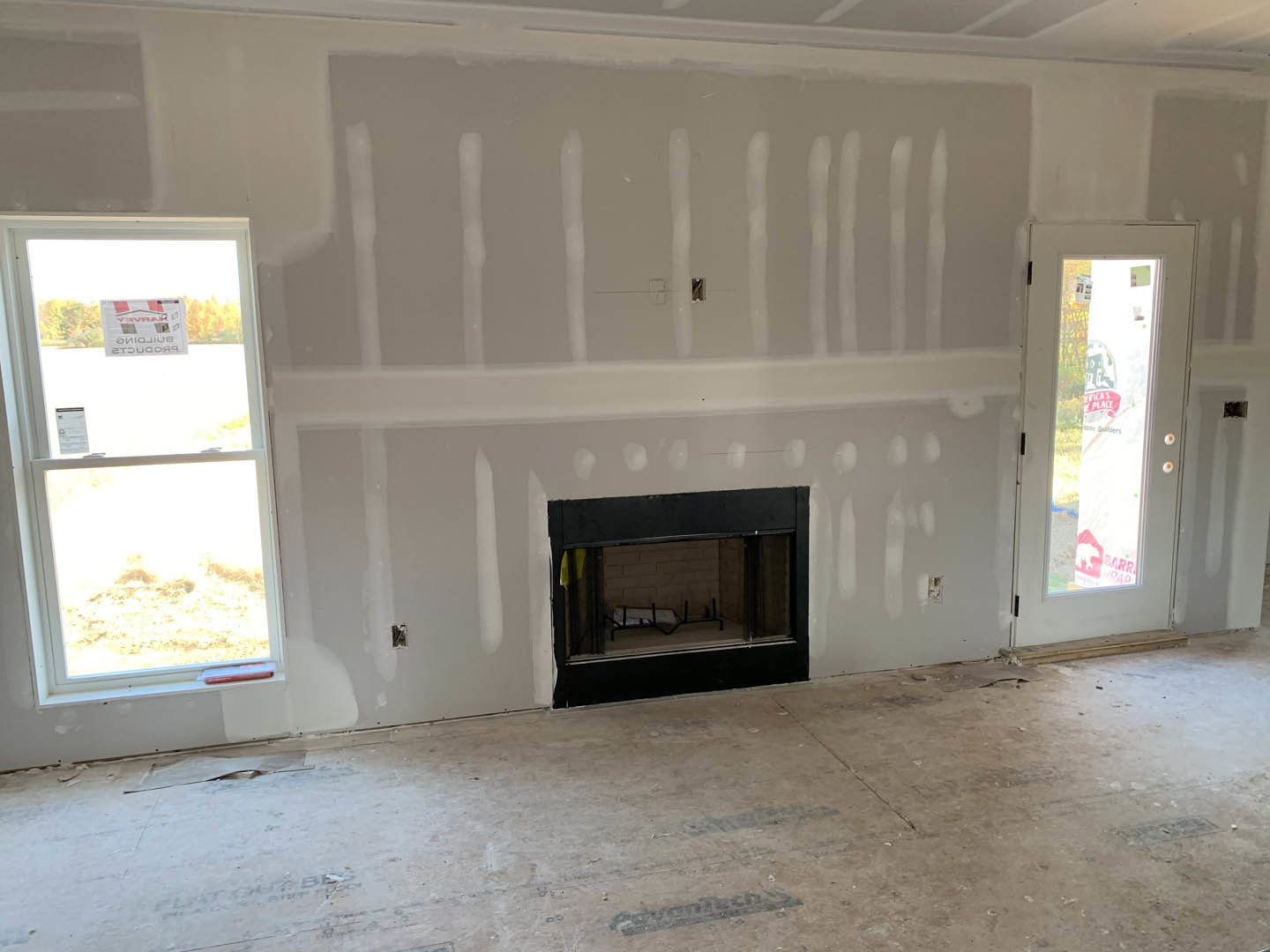 Living room with plaster walls, concrete floor with black paint, modern fireplace, door with window, and a window displaying a sign