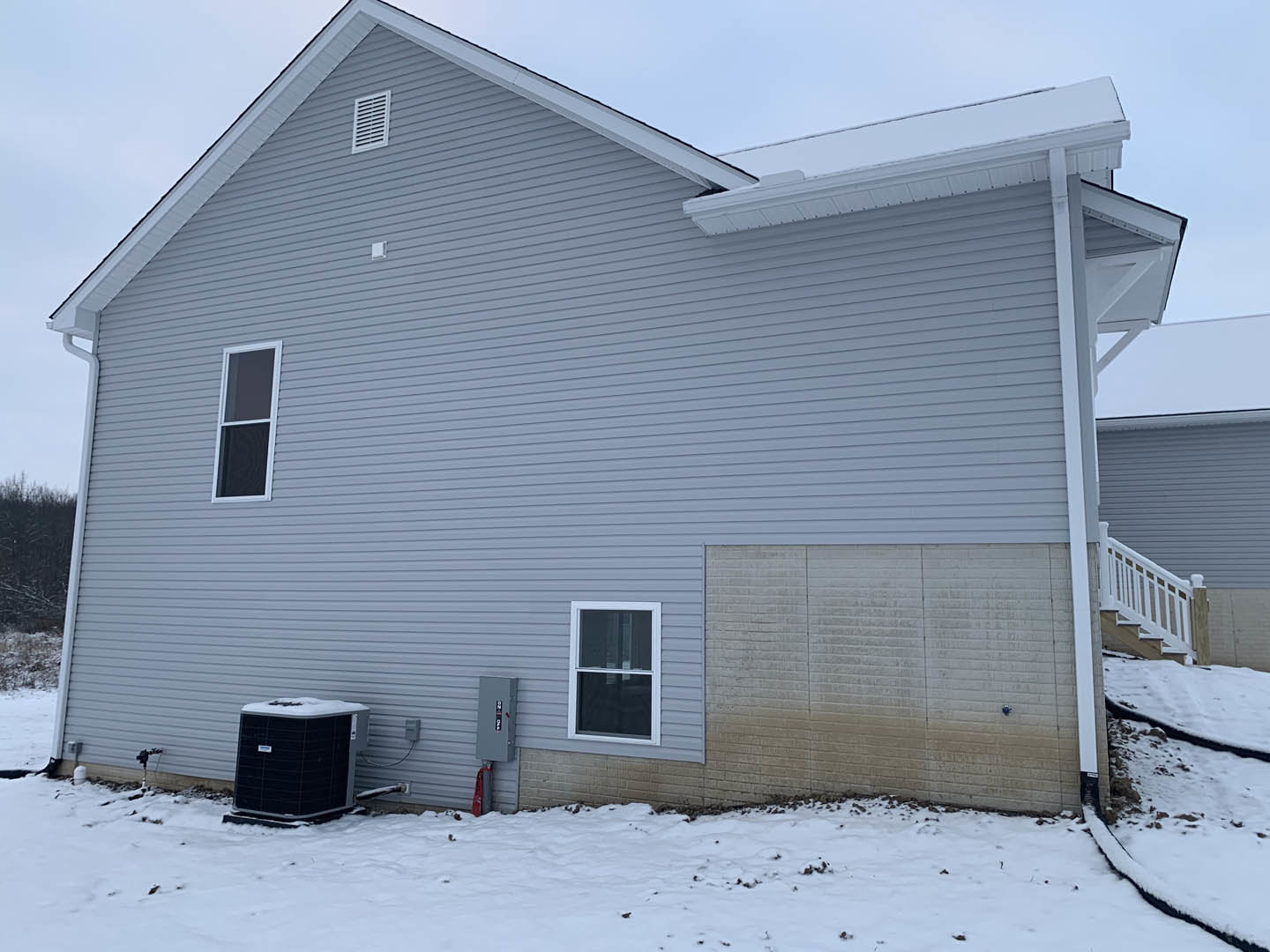 Two-story home with white siding, attached garage, white-framed windows, black and white heat pump, roof vent, and snow covering the ground