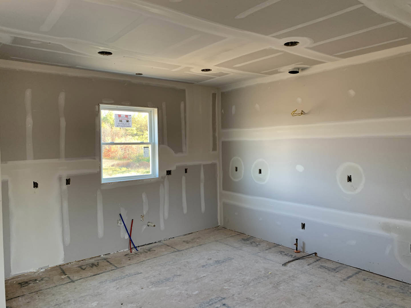 White-walled room with a window displaying a sign, exposed wires on the wall, white tile flooring with visible dirt, blue and red brush resting on the floor