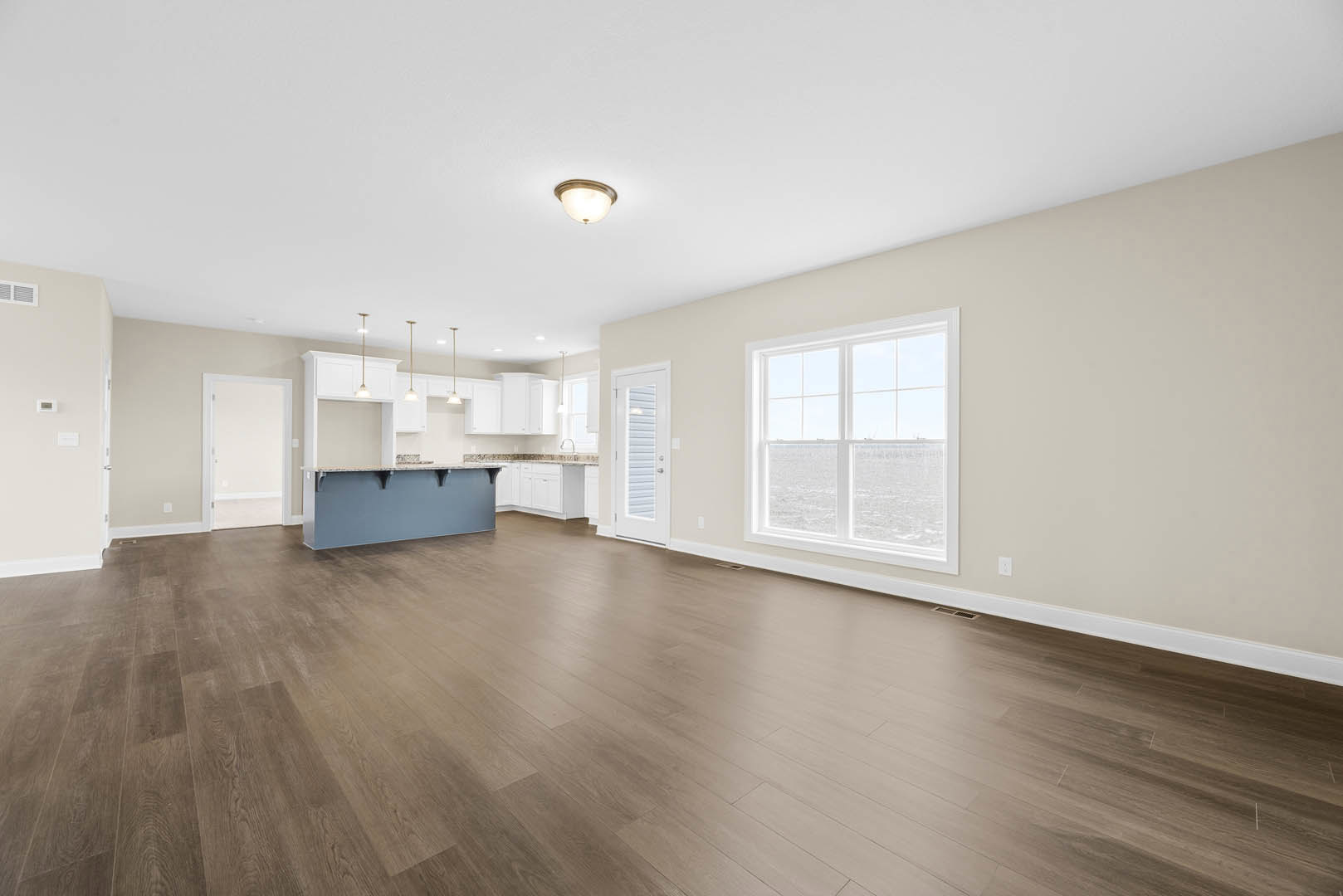 Open-concept kitchen with marble countertop, wood flooring, white cabinetry, ceiling light fixture, and large window overlooking the ocean.