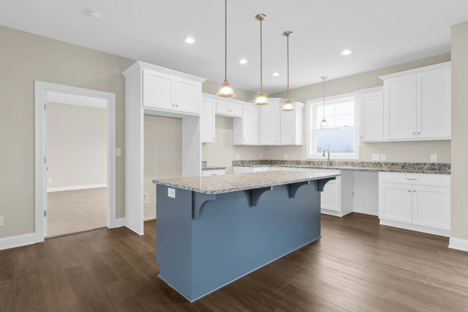 Blue kitchen island with marble countertop, white cabinets with silver handles, stainless steel sink, light wood flooring, and white ceiling.