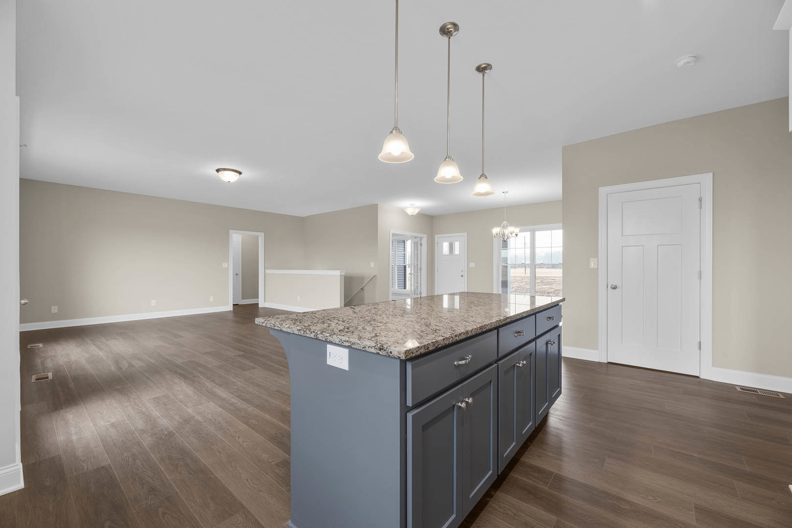 Granite kitchen island with built-in sink, white cabinetry, stainless steel appliances, light wood flooring, and a white door with silver knob