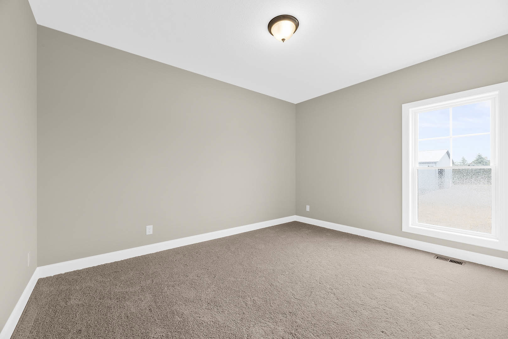 Carpeted room with white walls, large window overlooking neighboring house, ceiling light fixture, baseboard molding
