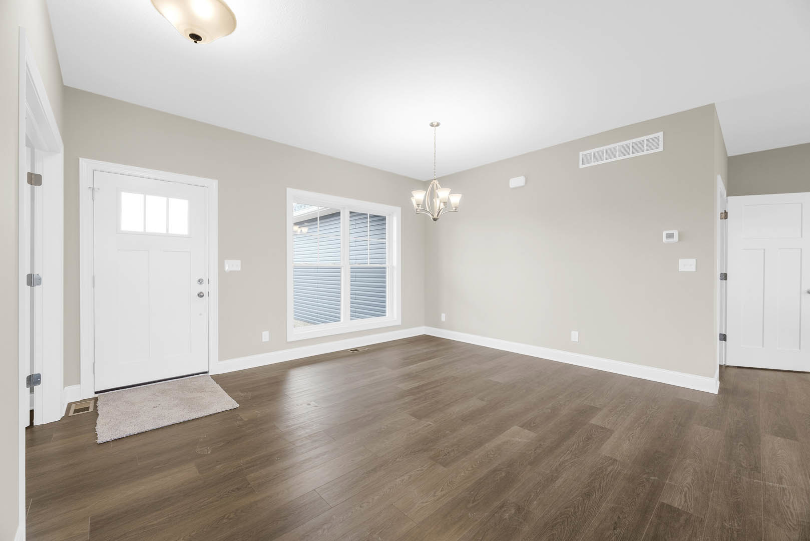 White paneled door with black handle, hardwood floor, plaster walls, and window in a residential interior.