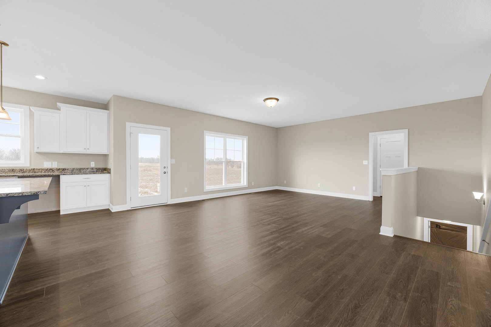 Wood floor room with white walls, ceiling light, white door and window overlooking grassy field