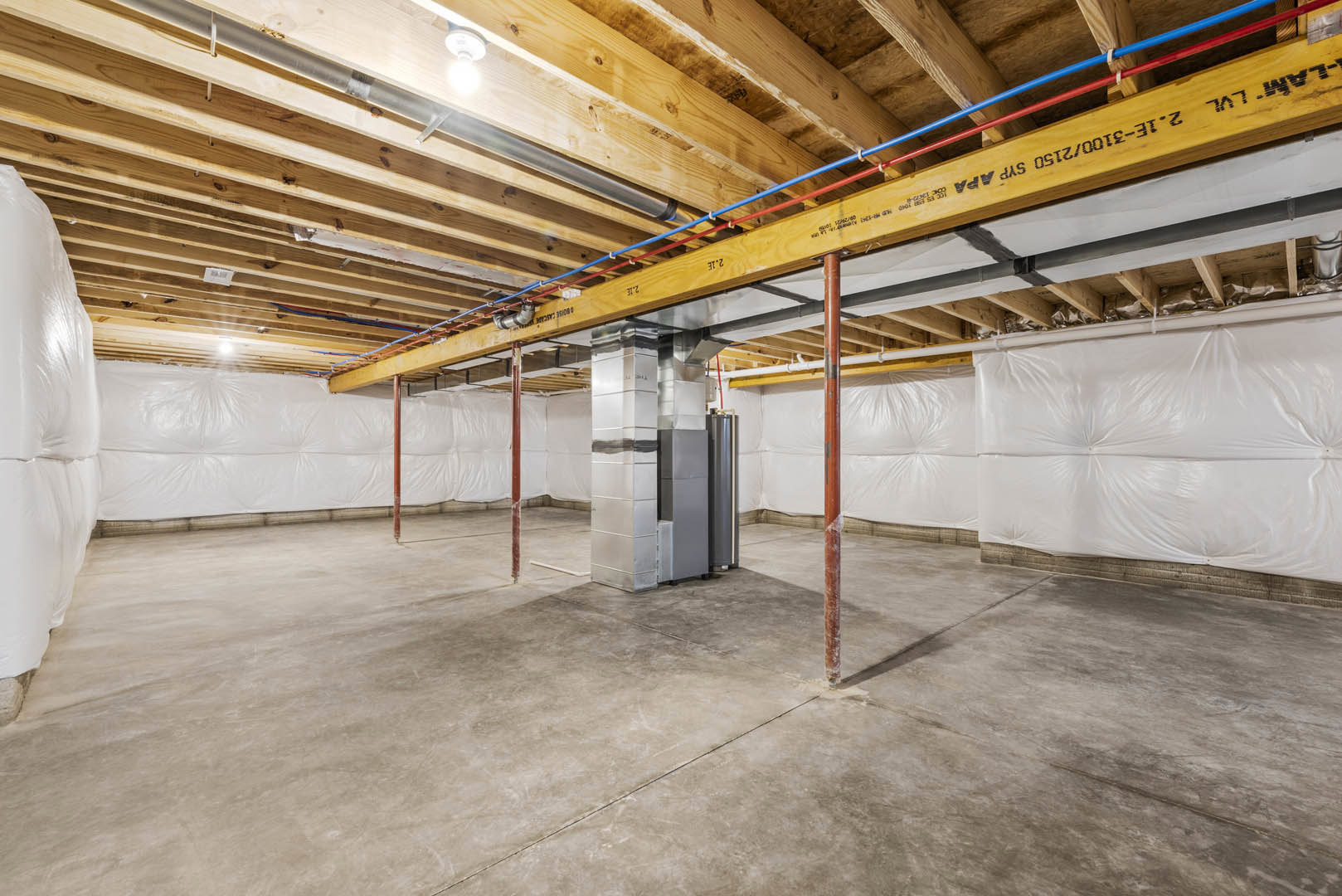 Basement room with exposed steel beams and metal pole, concrete floor, white insulated walls, visible ceiling pipes, and plastic wall covering