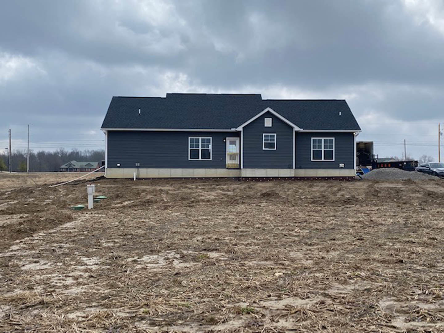 Partially built house with blue roof, white-framed windows, and exposed exterior walls, surrounded by a dirt field under a cloudy sky