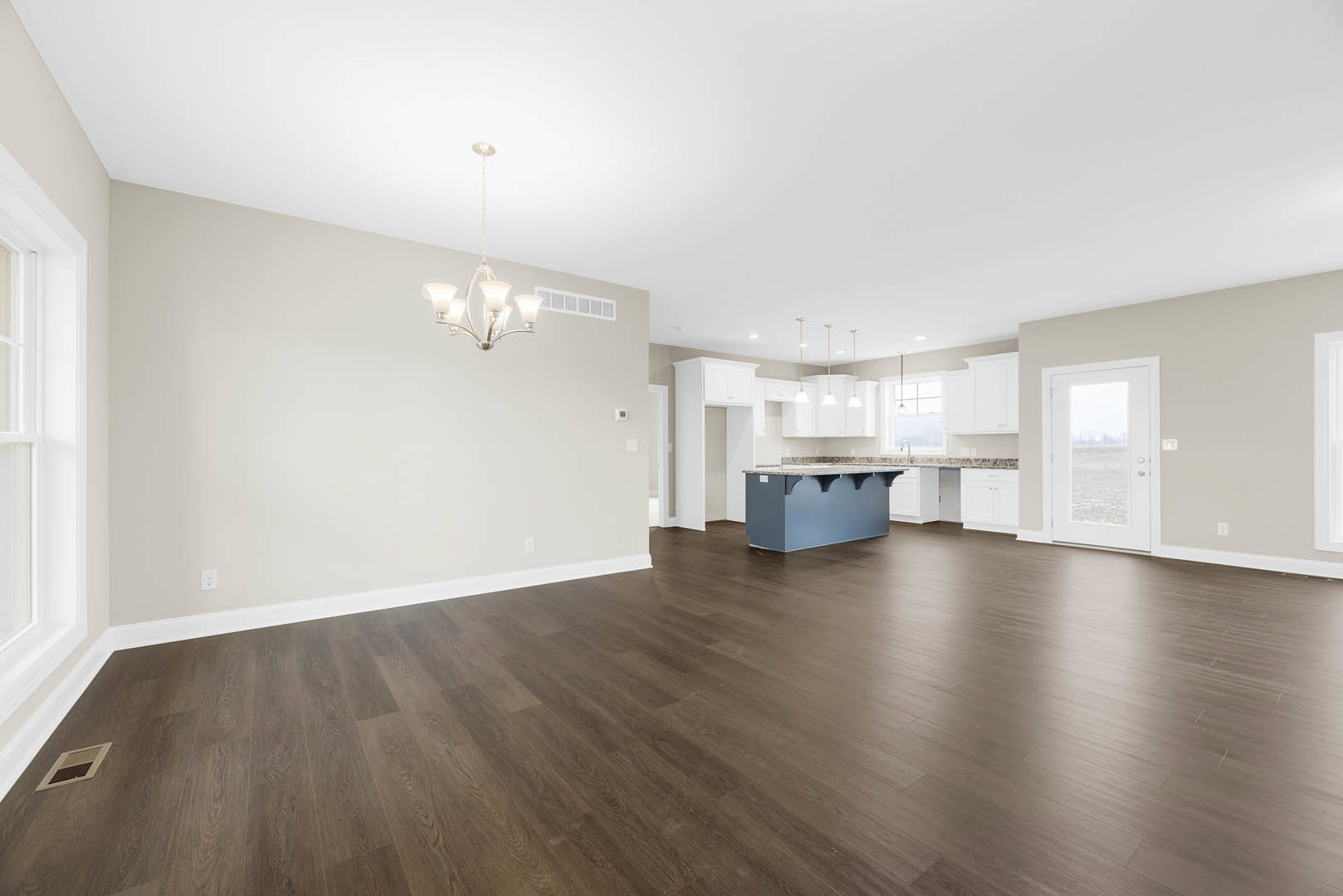 Open-concept kitchen featuring a marble-topped island, hardwood flooring, white plaster walls, chandelier with white shades, and a door framing an ocean view